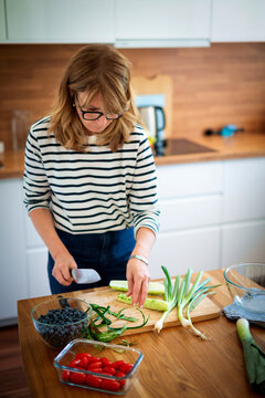 A middle-aged blonde woman standing in the kitchen and preparing organic salad