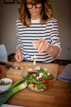 A middle-aged blonde woman standing in the kitchen and preparing organic salad