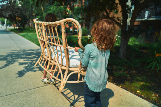 Two boys carrying a wicker loveseat down a sidewalk from behind