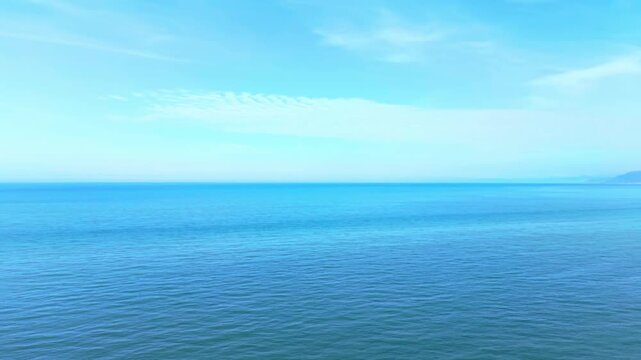 Smooth aerial pan moving right to left while slowly pulling back from the sea, ending with a scenic view of the island lighthouse and coastline.