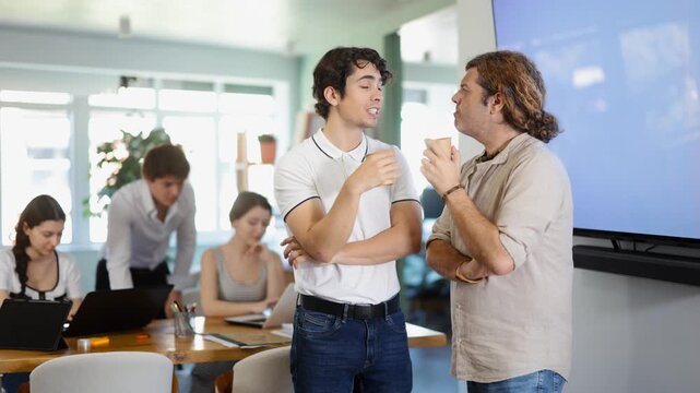 Two young men colleagues drinking coffee in office during break from work