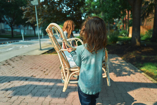 Two boys carrying a rattan loveseat along a brick sidewalk