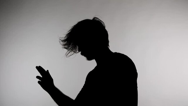 An anonymous silhouette of a man stands against a white background with his hair down and pretending to shoot a finger