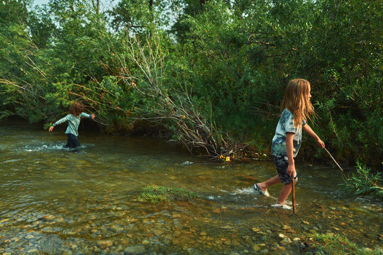 Two boys wading through a river with sticks