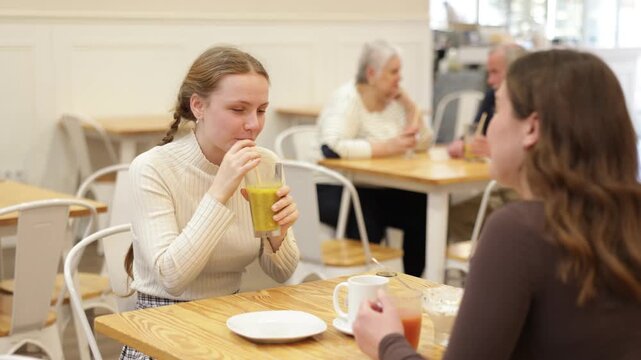 Teenage girl chatting with young woman talking at table in bright cafe while enjoying dessert and drink. Sisters met in the afternoon in a coffee shop