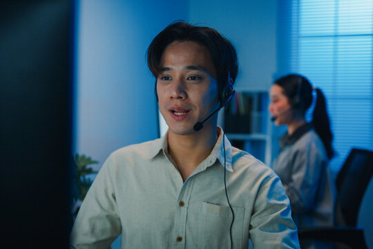 Gen z Asia young call center team or customer support service executive use computer and microphone headset work technical e commerce support in late night office. Telemarketing or sales job concept.
