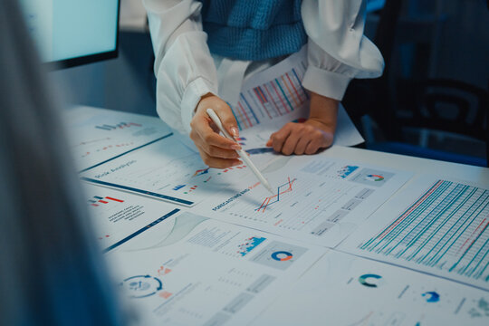 Close up Asia businesspeople meeting plan analysis statistics brainstorm and work with paperwork around table in office conference room at night. Business finance partners strategy investment success.