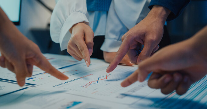 Close up Asia businesspeople meeting plan analysis statistics brainstorm and work with paperwork around table in office conference room at night. Business finance partners strategy investment success.