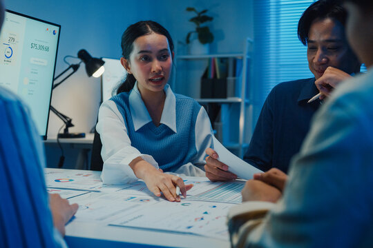 Asia businesspeople presentation sales meeting plan statistics brainstorm and work with paperwork around table in office conference room at night. Business finance partner strategy investment success.