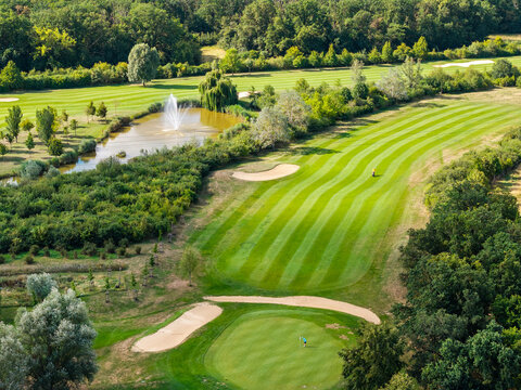 Aerial view of Magdeburg golf course shows striped fairways, sand bunkers, pond and fountain framed by dense woodland. Summer landscape combines sport, water, manicured lawns and lush greenery