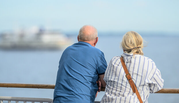 Senior couple watching calm sea from ferry deck railing.