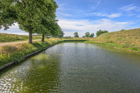 Peaceful moat water bordered by trees and grassy embankments.
