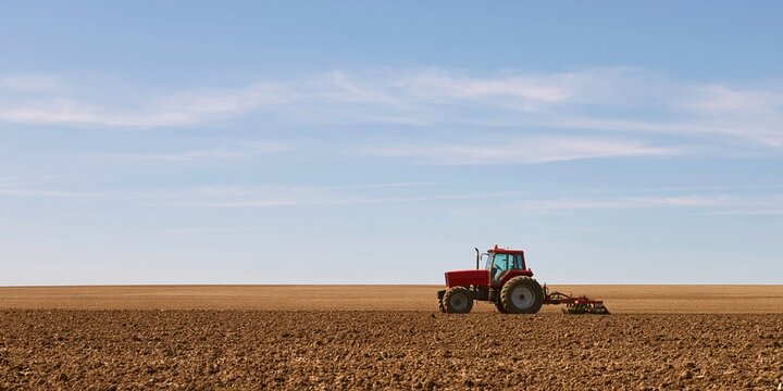 Tractor plowing brown field for agriculture farming and soil cultivation on land