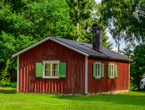 Red wooden cottage with green shutters in bright summer garden.