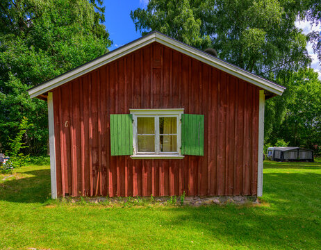 Front view of red wooden cottage with green shutters.