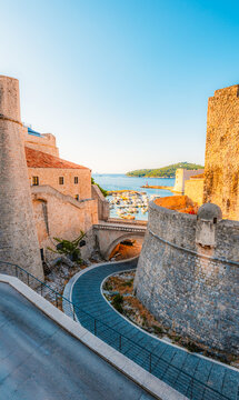 Old Port of Dubrovnik from the city walls, featuring historic stone fortifications and boats in the turquoise Adriatic Sea, Croatia.