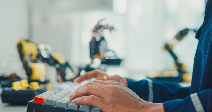 Close-up young Black female robotics engineer coding AI software for robotic arm in laboratory. Embedded system, firmware testing, machine learning, industrial automation, future technology concept.