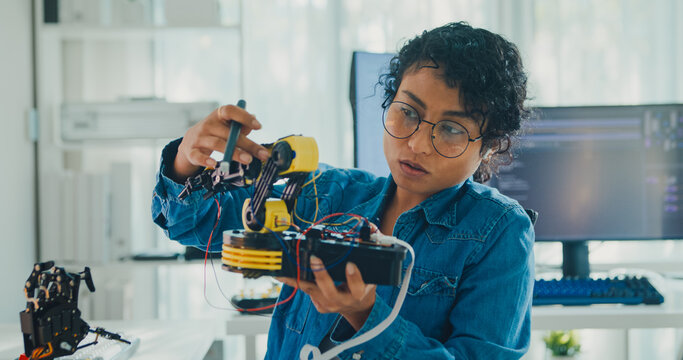 Young African American female robotics engineer discussing mechanical part on video call and looking at camera in laboratory. Remote work, virtual training, online meeting, future technology concept.