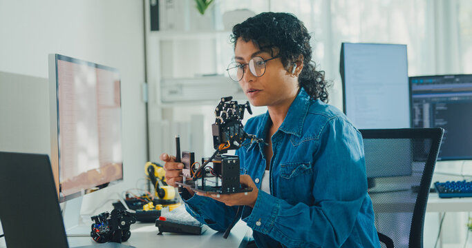 Young African American female robotics engineer discussing mechanical part on video call in laboratory. Remote work, virtual training, online meeting, future technology, technical support concept.