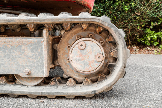 Ground level view of the rubber tracks of a small mechanical digger seen on a home driveway before being dug up. The sprockets for the tracks can be seen.