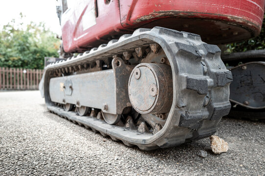 Ground level view of the rubber tracks of a small mechanical digger seen on a private driveway before being excavated. Part of the rear engine cowling can be seen.