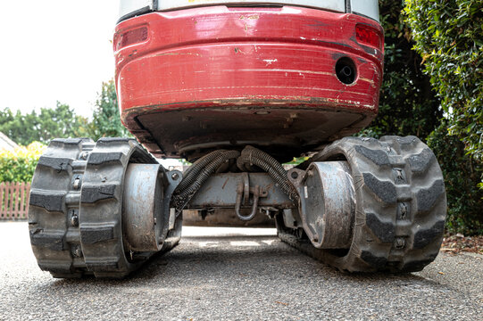 Unusual ground level view of a small mechanical digger and excavator showing the rear engine cowling and its small exhaust. The rubber tracks can be seen heavily worn.
