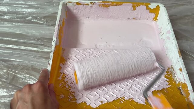 A woman's hand rolls rollers with packs of paint along a tray