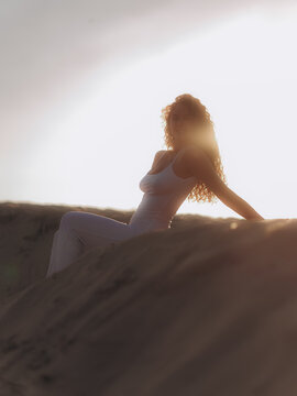 Woman Sitting on Sand Dune Backlit by Sunset