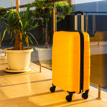 bright yellow stylish suitcase near a glass fence in a hotel.