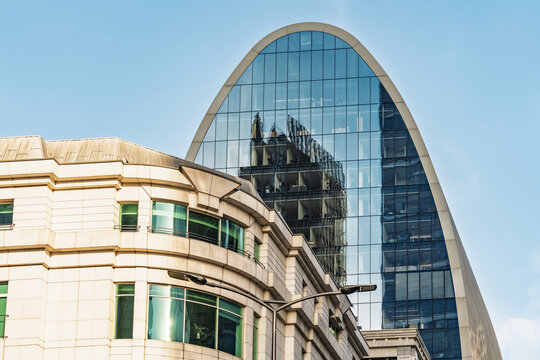 View of the modern glass facade of The Scalpel skyscraper reflecting the surrounding urban architecture against a clear blue sky in London, England, United Kingdom.