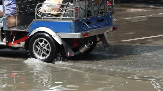 A traditional motorized tricycle - tuk tuk drives through a puddle on a street