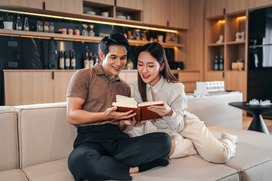 Happy couple reading book together on sofa in modern home interior enjoying leisure time sharing knowledge learning education lifestyle relaxation bonding