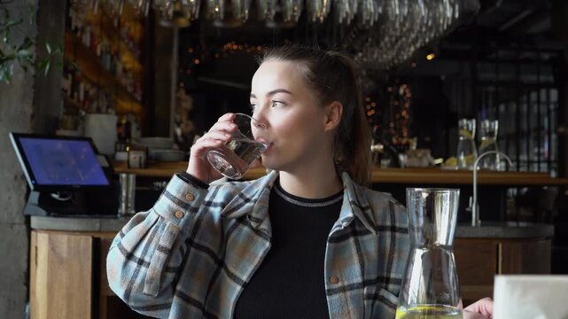 young girl drinks water in restaurant and looks out the window, woman holds glass of water and takes sips in cafe