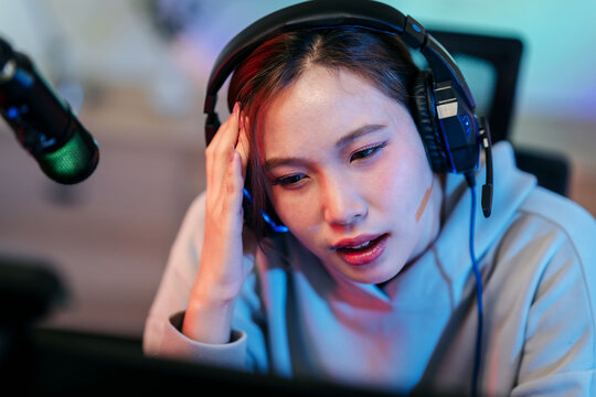 Professional female streamer gamer experiencing stress during live online gaming broadcast at home studio setup