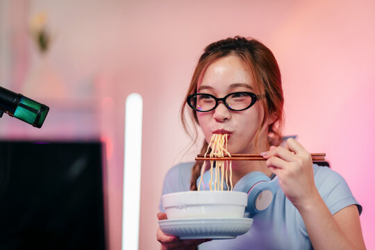 Professional streamer gamer eats delicious instant noodles chopsticks modern home studio setup live broadcast gaming break pink background