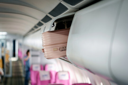 Traveler stows carry on suitcase in airplane overhead bin during boarding preparing for flight journey vacation or business trip aboard commercial aircraft