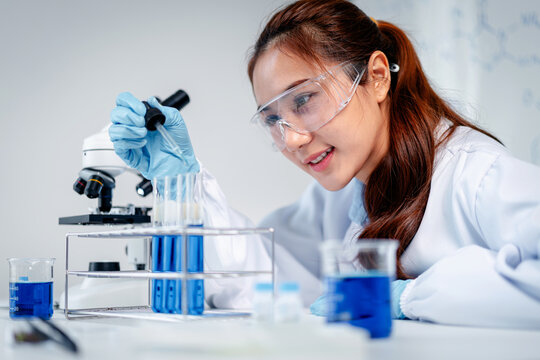 Dedicated scientist meticulously conducts laboratory experiments with blue chemical solutions utilizing a microscope for advanced research discovery