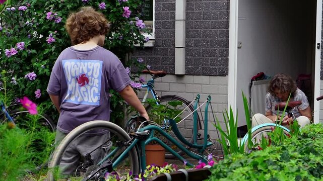 Father and son repairing upside‑down bicycle outdoors near blooming hibiscus