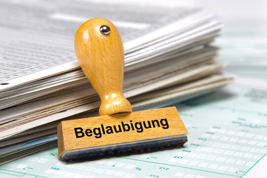 In einem B&uuml;ro lehnt ein Holzstempel an einem Stapel Papiere mit der Aufschrift: Beglaubigung