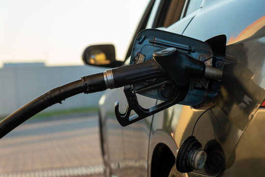 Close-up of a fuel nozzle refilling a car at a gas station, captured in natural light, highlighting energy and transportation concepts.