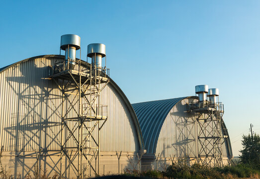 Modern industrial warehouses with metal vents and curved roofs, captured in soft morning light under a clear blue sky.