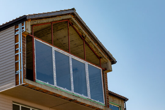 Unfinished house balcony with exposed steel frame and large glass windows under clear blue sky, ideal for renovation or real estate concepts.
