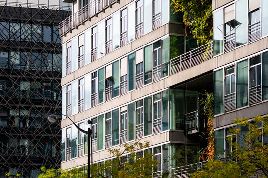 Sunlight falls across an office facade of glass and windows, while balcony greenery softens the modern architecture and its corporate presence in the urban block.