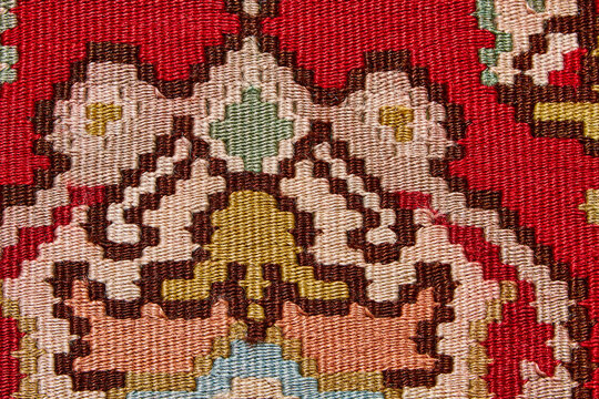 Traditional woven wool kilim pattern texture featuring intricate designs in vibrant colors, including red, pink, green, and beige, showcasing detailed craftsmanship and textile artistry