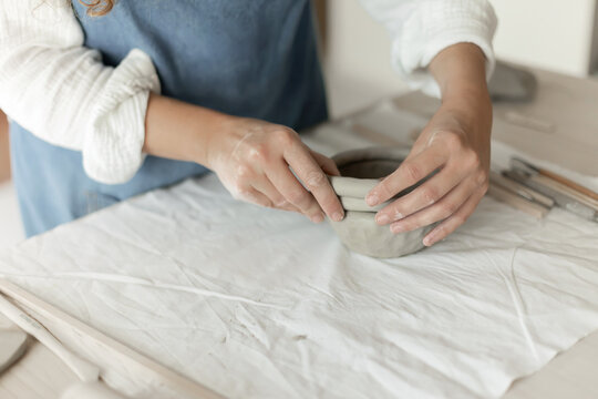 Woman potter meticulously shaping clay in a studio setting, demonstrating a creative and focused approach, captured in a close-up side view, the scene showcases.