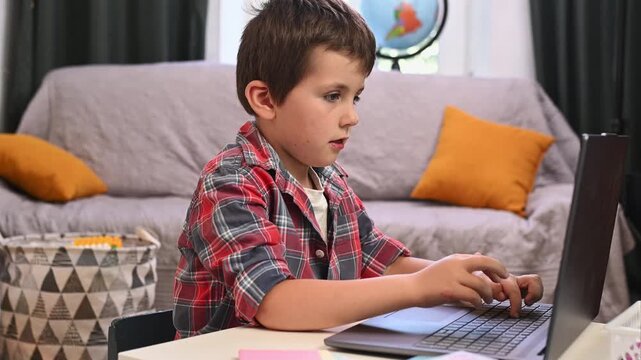 A 6-year-old boy is learning to type on a laptop and is sitting in the living room doing his homework.