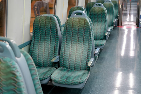 Row of upholstered seats inside a passenger train cabin on a bright day with empty spots for commuters to sit during their daily trip to the city center