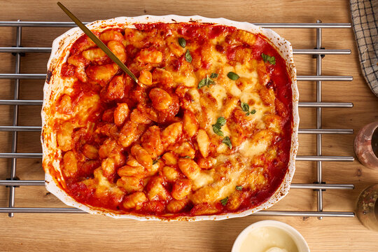 Baked gnocchi with tomato sauce, cheese and basil in casserole dish with serving spoon