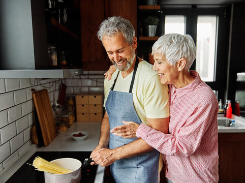 Portrait of happy senior mid aged mature couple prepering meal with fresh vegatebles in kitchen at hpme