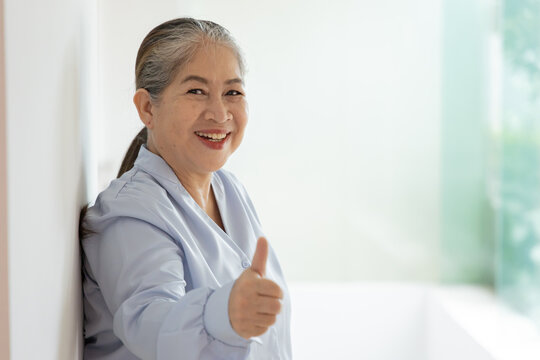 Happy smiling Asian silver generation old woman showing approving, passing, good, yes, go for it, good to go, one thumb up hand gesture, indoor scene